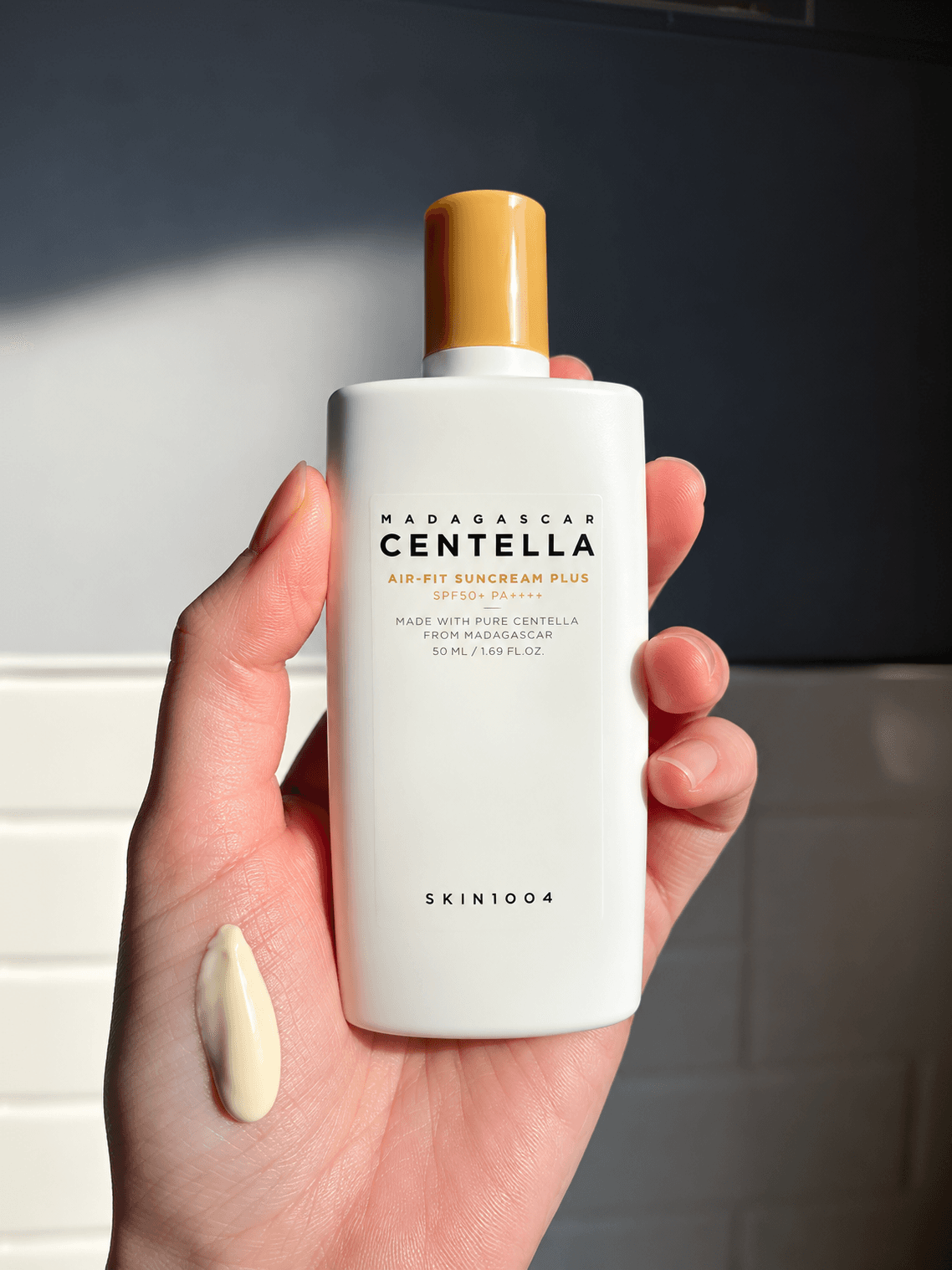Hand holding a Madagascar Centella sunscreen bottle